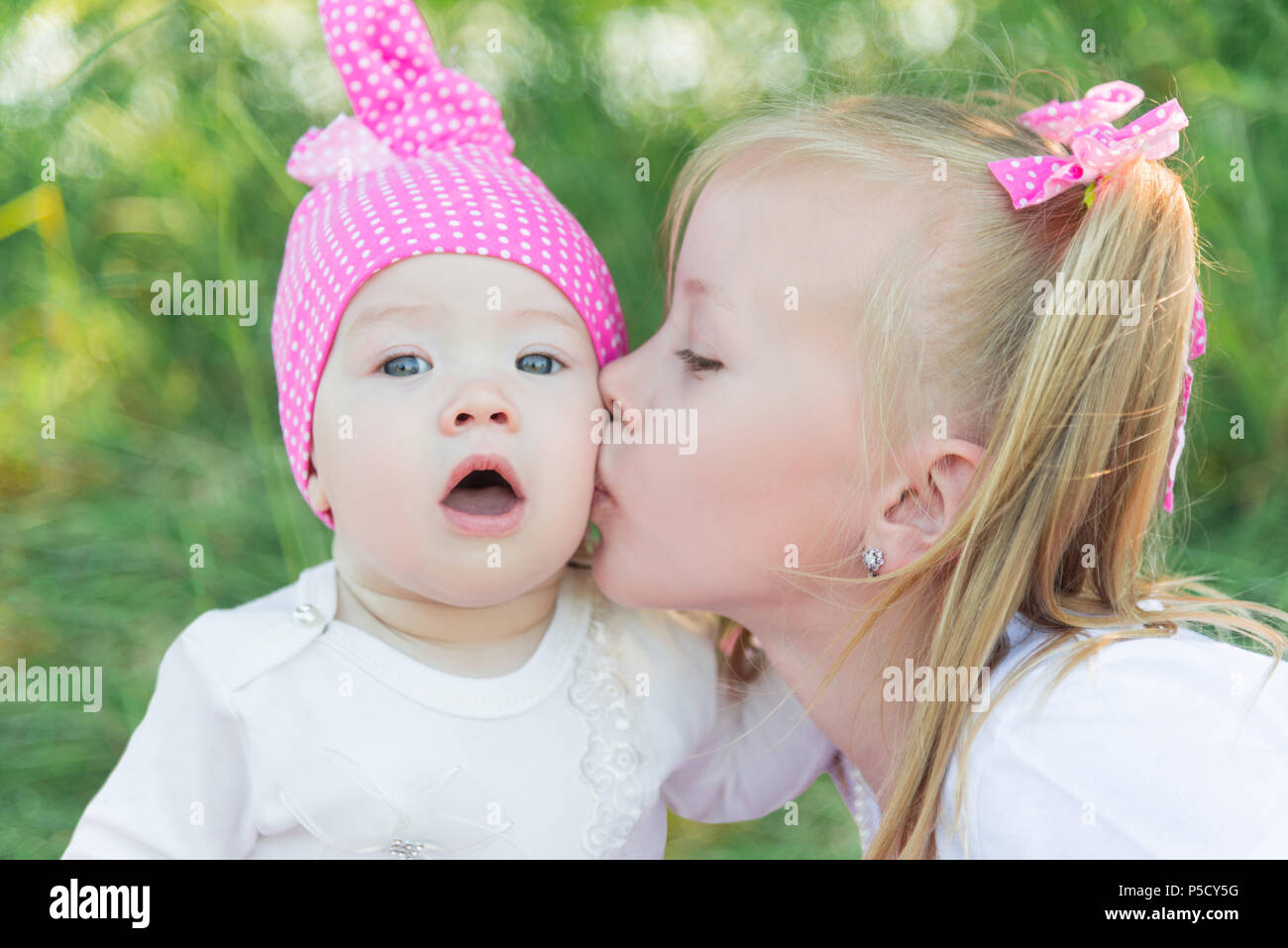 Deux soeurs. La grande sœur la plus jeune sœur de baisers sur la joue. Pink hat dans un PEA et d'arcs. Banque D'Images