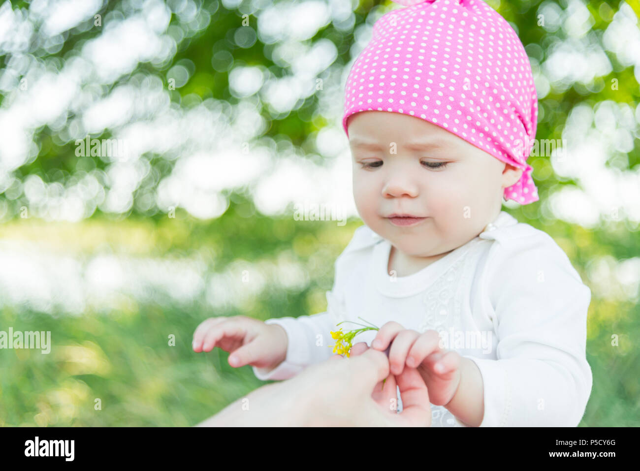 Enfant souriant dans l'herbe. Chapeau à pois blancs. L'herbe verte. Enfant souriant. L'enfant prend une fleur. Banque D'Images