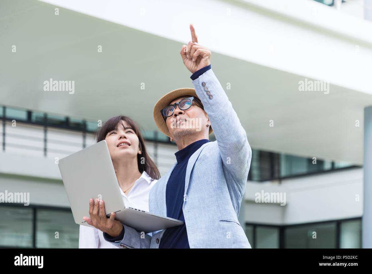L'architecte senior mâle pointant sur l'immeuble et de parler à sa femme le personnel subalterne à leur projet tout en maintenant son ordinateur portable Banque D'Images