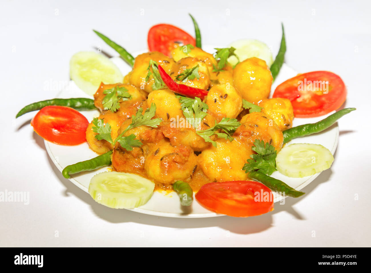 La nourriture végétarienne indienne épicée préparée avec des petites pommes de terre connue sous le nom de Dum Aloo garnie avec le concombre, la tomate et le piment vert. Banque D'Images