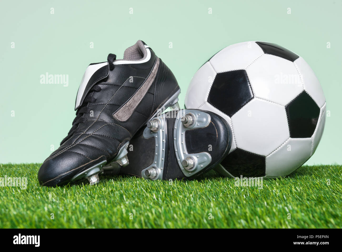 Chaussures de football ou de football et le ballon sur l'herbe avec un fond vert. Banque D'Images