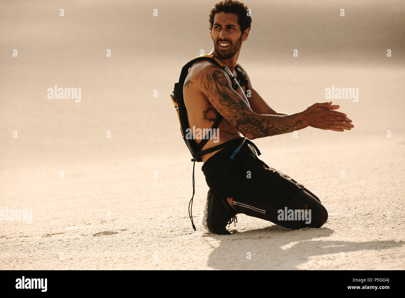 Homme musclé se reposant sur une dune de sable et frottant ses mains mouillées avec du sable pour sécher. homme de fitness prenant une pause après l'entraînement en plein air. Banque D'Images