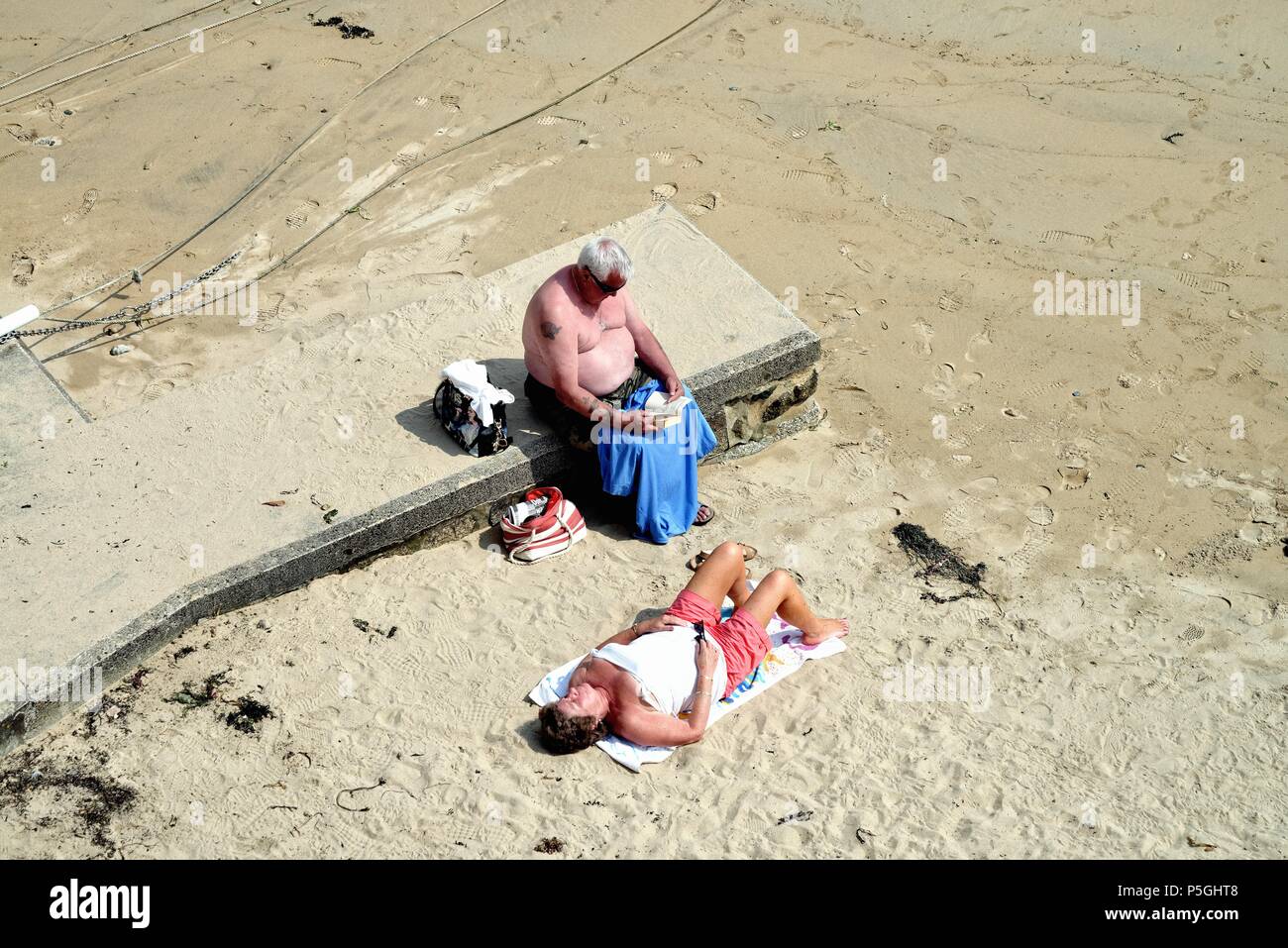 Personnes âgées couple obèses à bronzer sur la plage de Cornouailles sur un jour d'été,Cornwall England UK Banque D'Images
