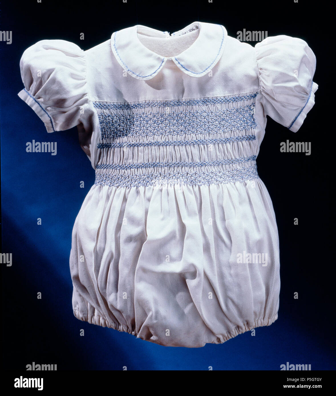 . Remarque : à des fins documentaires la description originale a été conservé. Corrections des faits et d'autres descriptions sont encouragés séparément de la description initiale. Barnkolt. Barnkolt bomullspiké puffärmar vit av med, ca 1947. Svenska : Kolt, helskuren bomullspiké vit av med liten rundsnibbig likaledes krage kort ärm. Isydd puffärm ärmlinning 10 mm med med broderad bård bred med stjälkstygn ljusblått med silke. Samma bård kantar kragen. Bröstpartiet med ett 105 mm brett smockbroderi ljusblått med silke. Nederdelen rynkade, byxorna, och med nederkanten puffade gummiband je. Knäppnin Banque D'Images