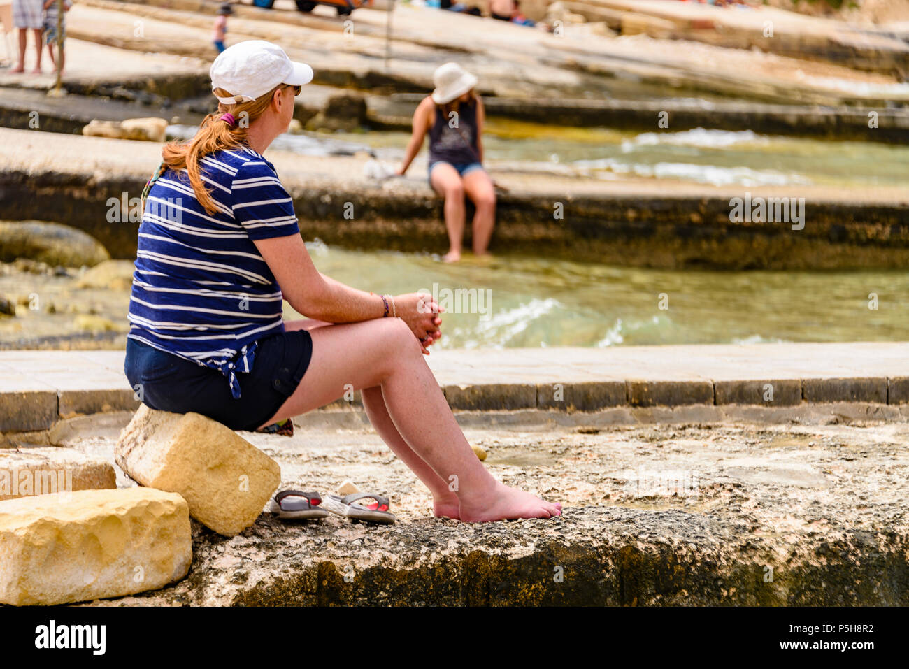 Deux femmes sont assises sur les jetées à Dwerja, la mer intérieure, Gozo, Malte. Banque D'Images