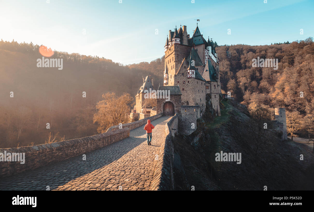 Randonneur marchant vers célèbre château Eltz allumé dans la belle lumière du matin au lever du soleil avec des reflets, Rheinland-Pfalz, Allemagne Banque D'Images