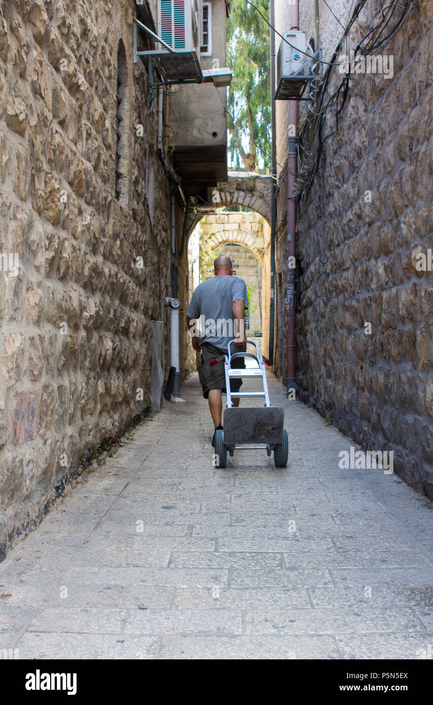 Un arabe homme tirant un petit chariot d'une petite rue latérale dans le souk de la vieille ville fortifiée de Jérusalem Banque D'Images