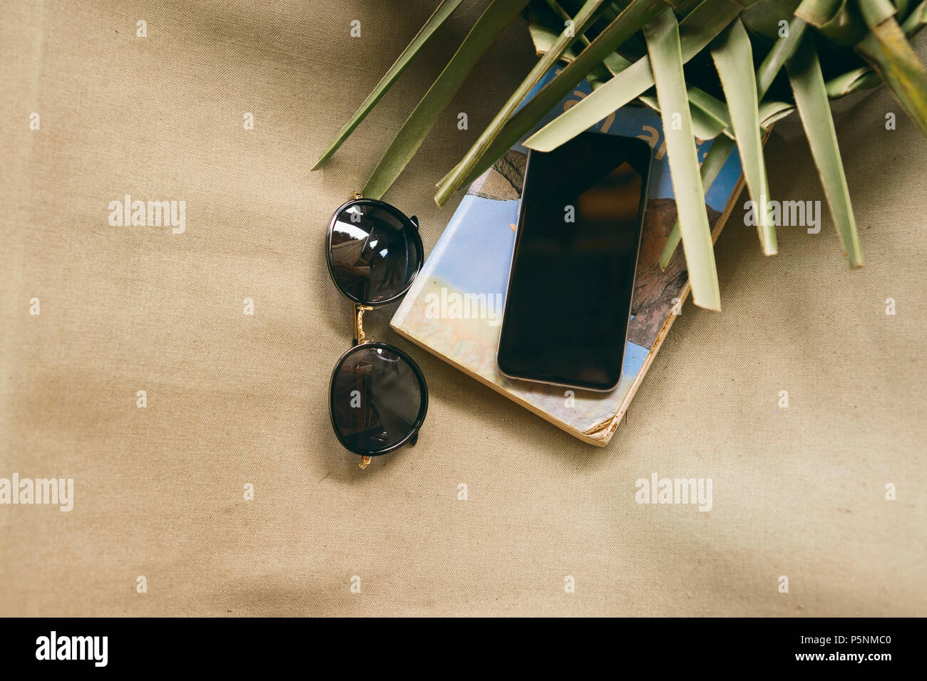 Téléphone avec réserve, lunettes de soleil et de feuilles de palmier sur une vieille chaise longue. Concept de vacances d'été Banque D'Images