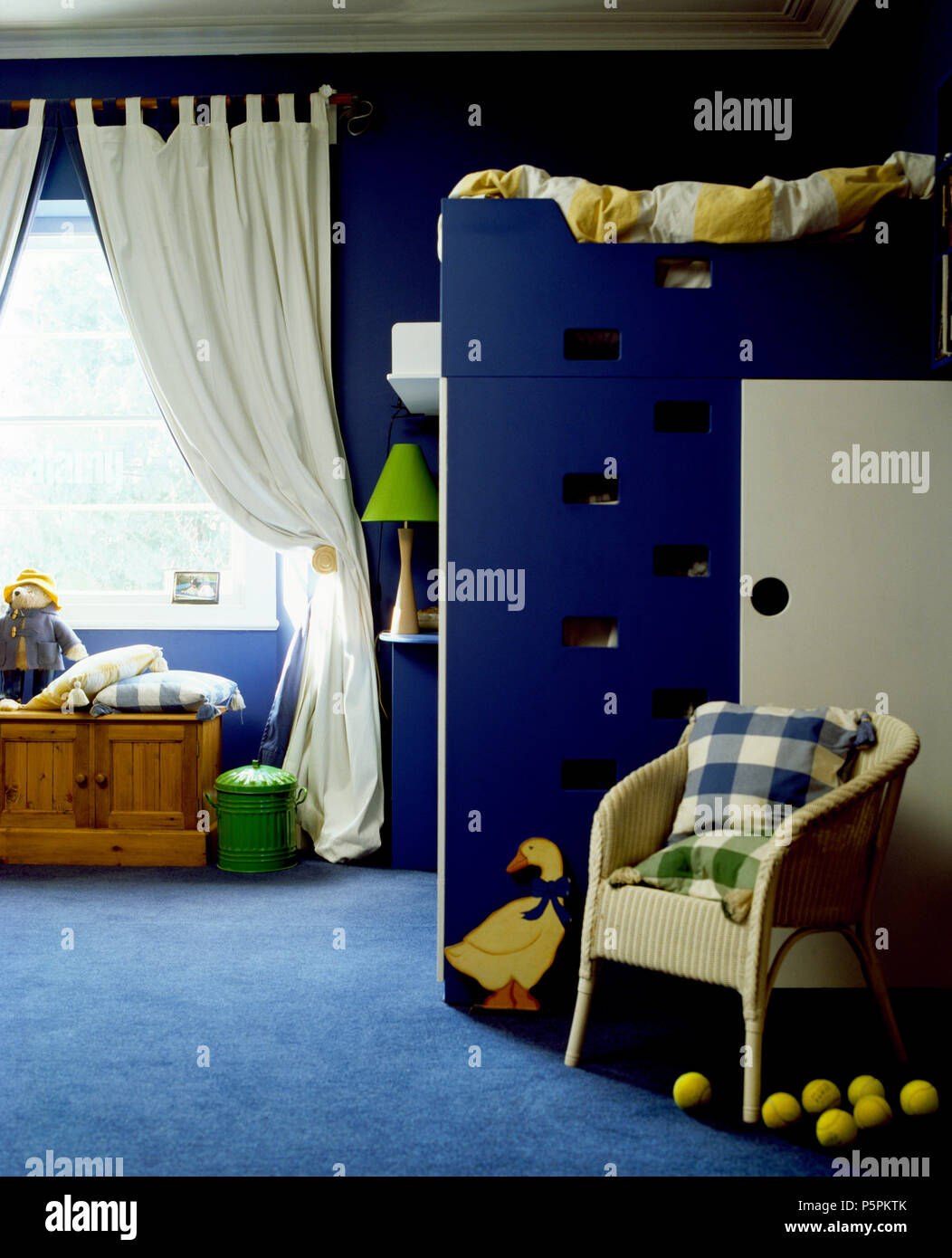 Lloyd Loom blanc chaise devant ofbunk d'appoint dans la chambre bleue avec des tapis bleus et des rideaux blancs Banque D'Images
