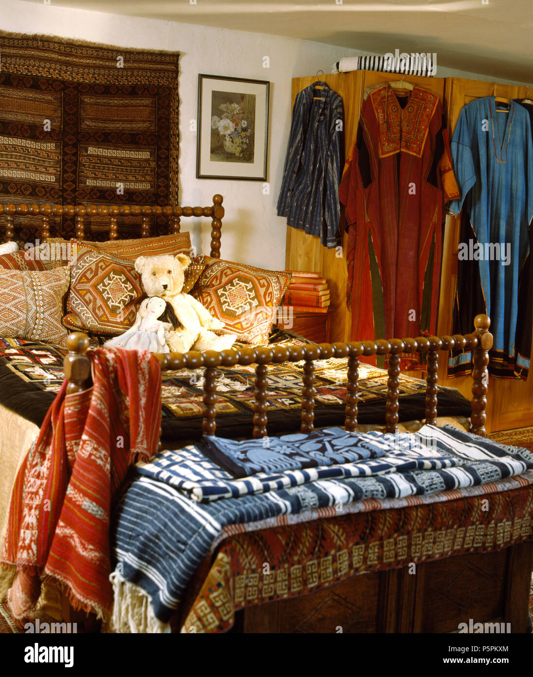 Accrocher de mur au-dessus de lit avec des supports en bois tourné avec des coussins empilés dans la chambre pleine de robes ethniques et tapis Banque D'Images