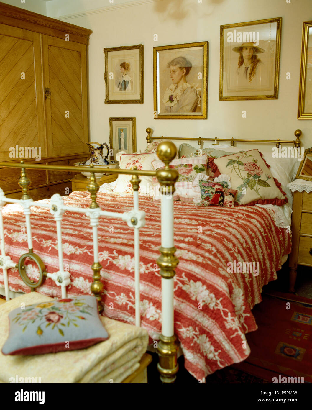 Vintage photos sur mur au-dessus de lit en laiton victorien avec red +couette et coussins blancs floraux en chambre cottage Banque D'Images
