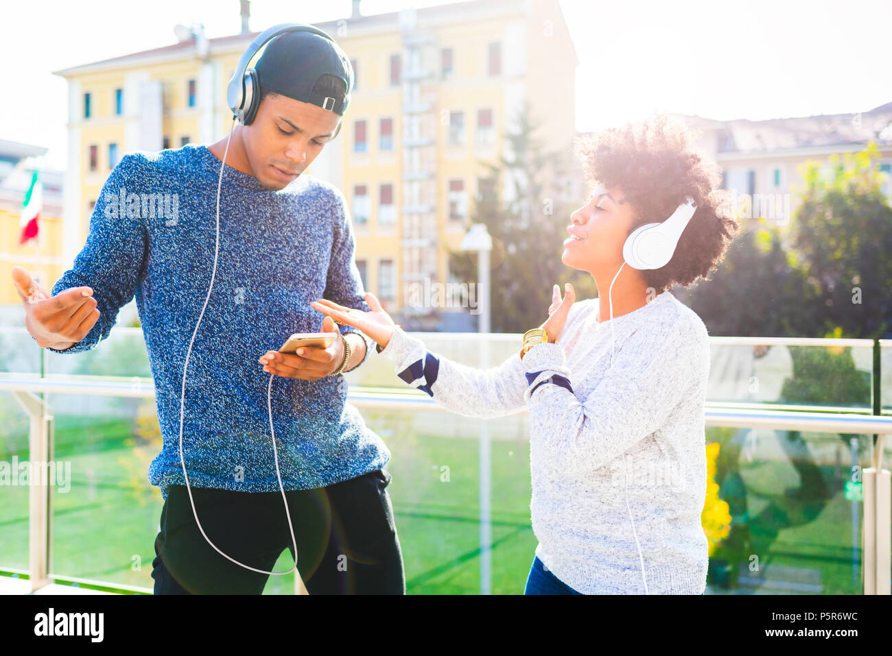 Jeune couple danse musique écoute multiraciale retour à l'extérieur de l'utilisation des écouteurs légers et smart phone - le bonheur, la technologie, l'interaction concept Banque D'Images