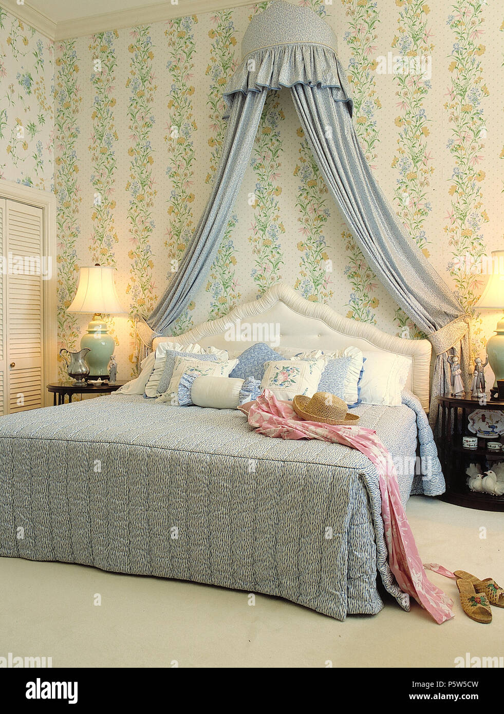 Coronet avec rideaux bleu au-dessus de lit king size dans la chambre avec un papier peint fleuri vert et lampes allumées Banque D'Images