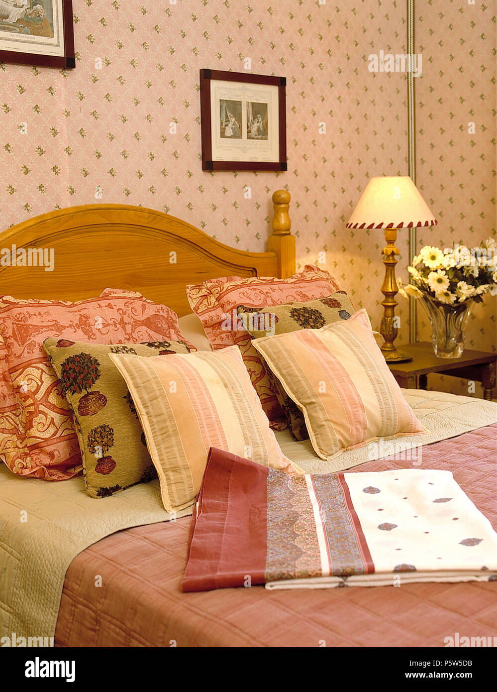 Coussins sur Pine avec lit double dans la chambre rose à motifs papier peint et lampe allumée Banque D'Images