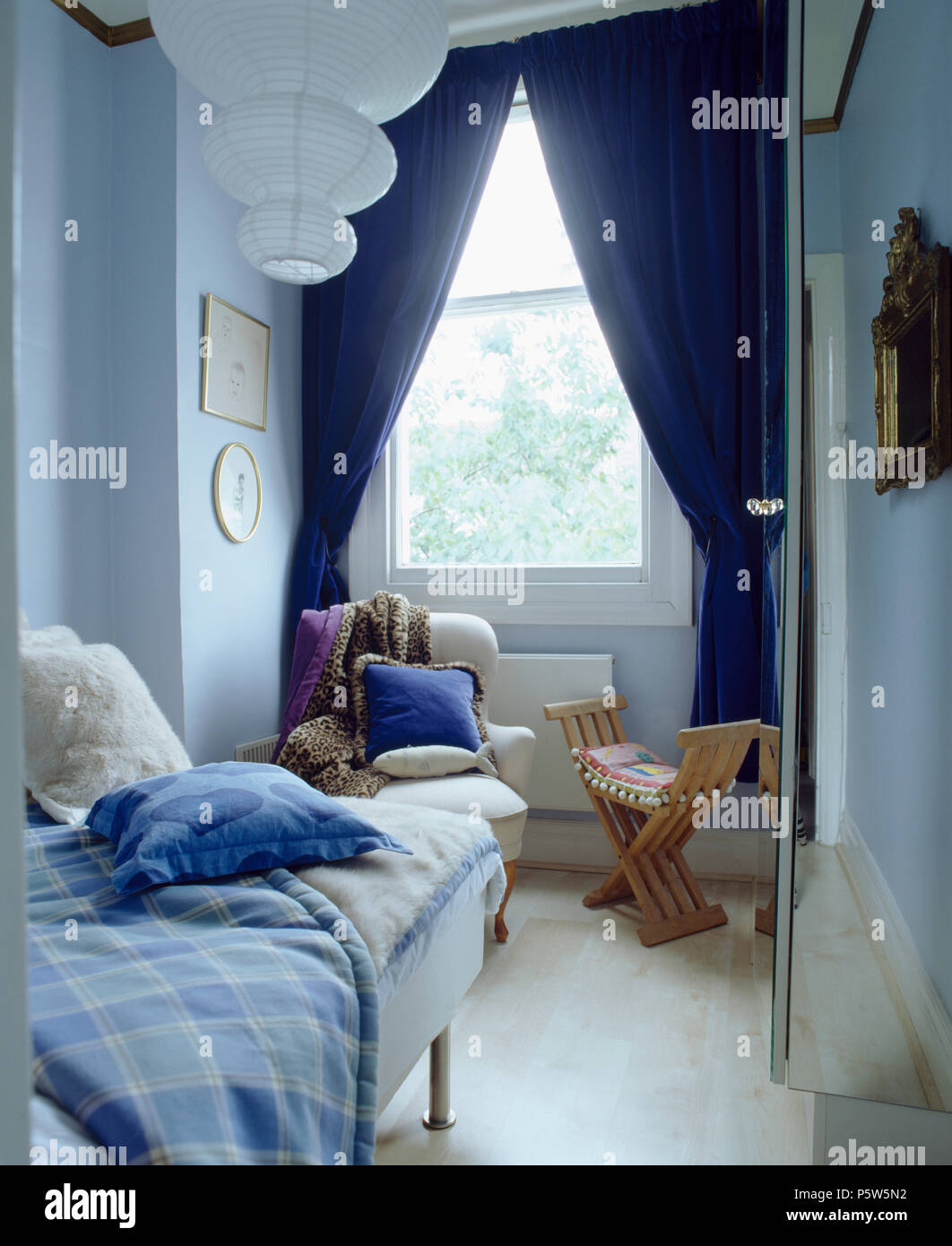 Rideaux bleu foncé sur la fenêtre dans une chambre étroite withg lit simple et d'un abat-jour de papier à plusieurs niveaux Banque D'Images