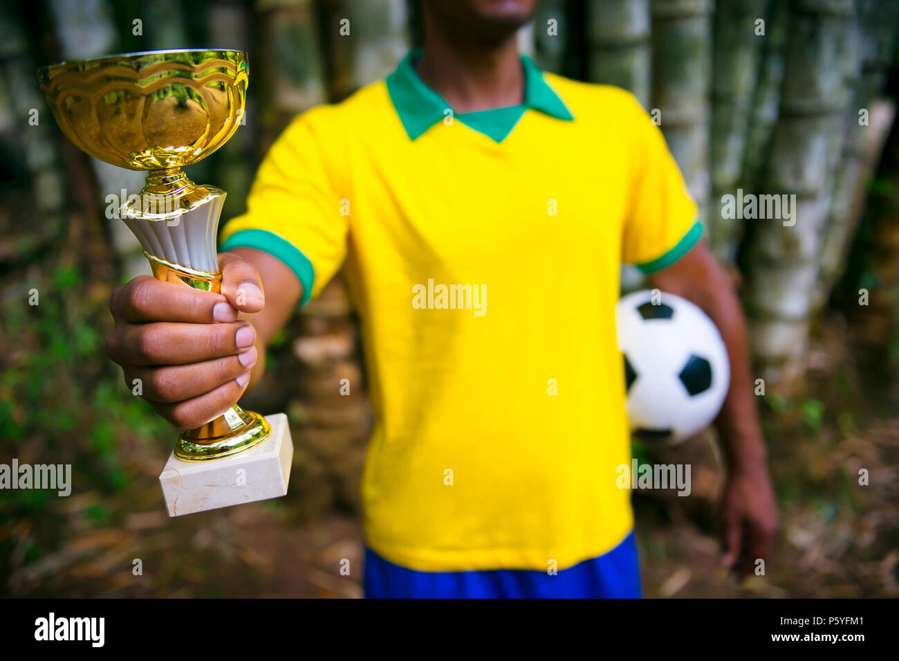 Brazilian soccer player est en style vintage maillot de football tient un trophée et d'une balle en face de bambou tropical jungle background Banque D'Images