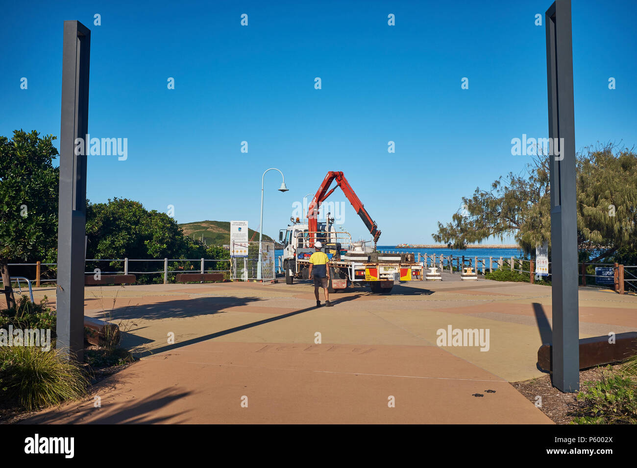 Un camion et son chauffeur le déchargement des bornes avec une grue pour empêcher l'accès des véhicules à la jetée, la plage de la jetée, Coffs Harbour, Nouvelle-Galles du Sud, Australie Banque D'Images