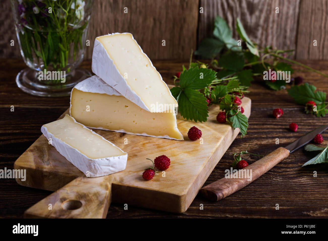 Fromage brie française, les fraises des bois et blanc bouquet de fleurs sauvages mauves sur table en bois en milieu rural Banque D'Images
