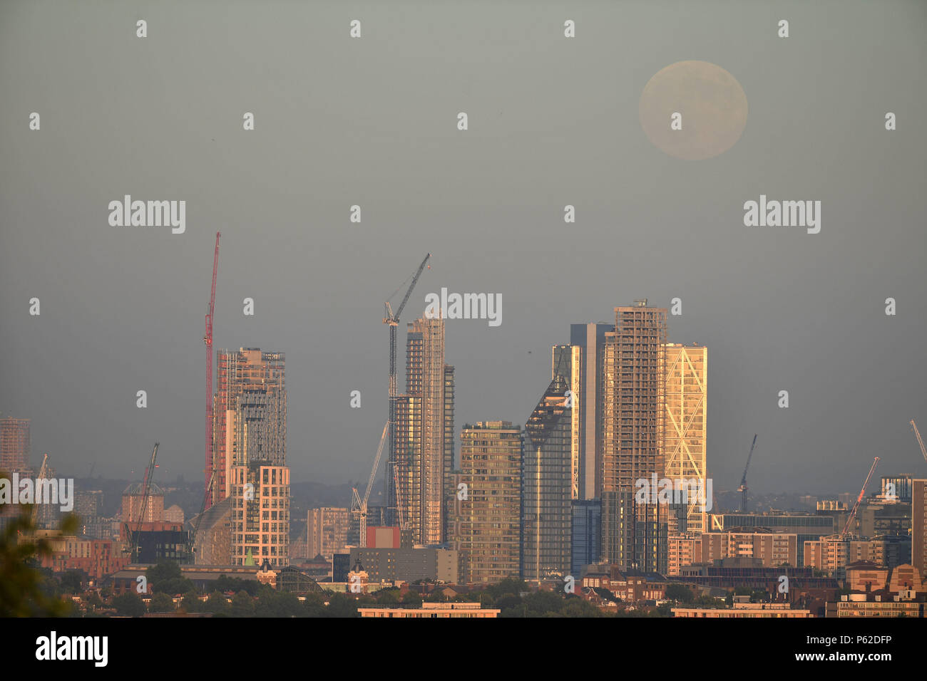 La vue depuis la colline du Parlement, à Hampstead, Londres de la Lune se levant au-dessus de la ville de Londres, l'avant de la Pleine Lune dans les premières heures du jeudi matin, qui est connu comme une fraise Lune. Banque D'Images