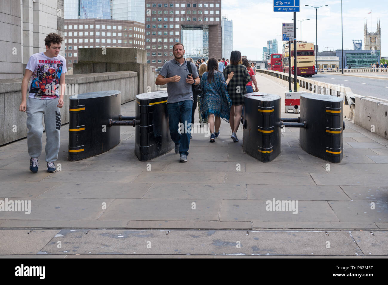 Les piétons passent par les barrières anti-terroristes de défense contre les attaques de véhicules sur le London Bridge, Londres, Angleterre, Royaume-Uni Banque D'Images