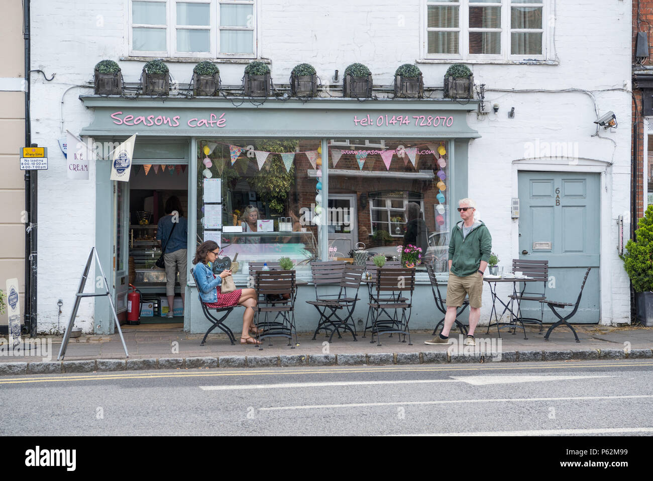 Femme assise à la table de la chaussée et l'homme debout à l'extérieur de Seasons Cafe Deli dans la place du marché, la vieille ville, Amersham Buckinghamshire, Angleterre, Royaume-Uni Banque D'Images