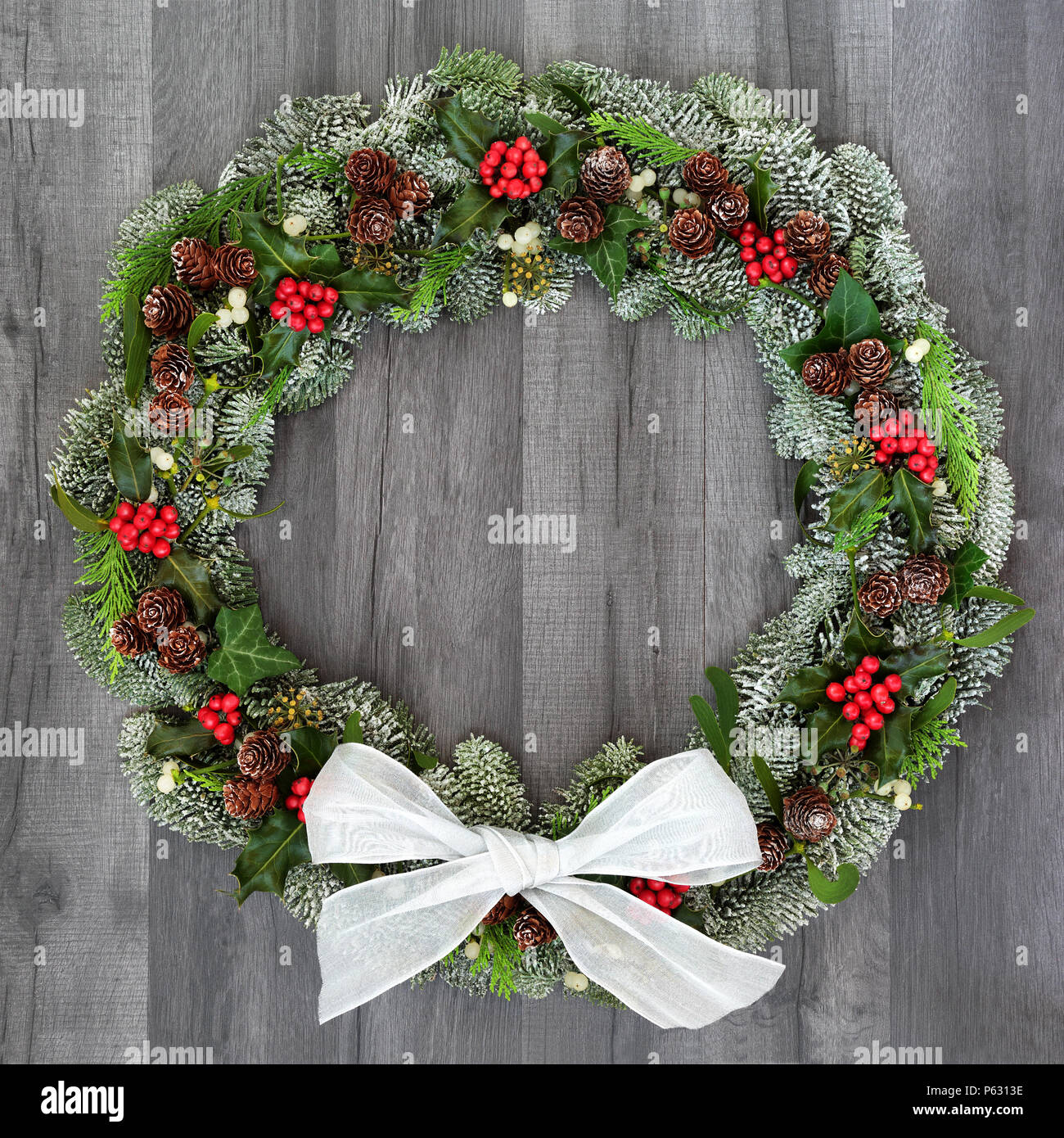 L'hiver et Noël traditionnel couronne naturelle de l'arc, houx, sapin epicea pin couvert de neige, le gui, pommes de pin, de cèdre et de feuilles de lierre rustique sur g Banque D'Images L'hiver et Noël traditionnel couronne naturelle de l'arc, houx, sapin epicea pin couvert de neige, le gui, pommes de pin, de cèdre et de feuilles de lierre rustique sur g Banque D'Images