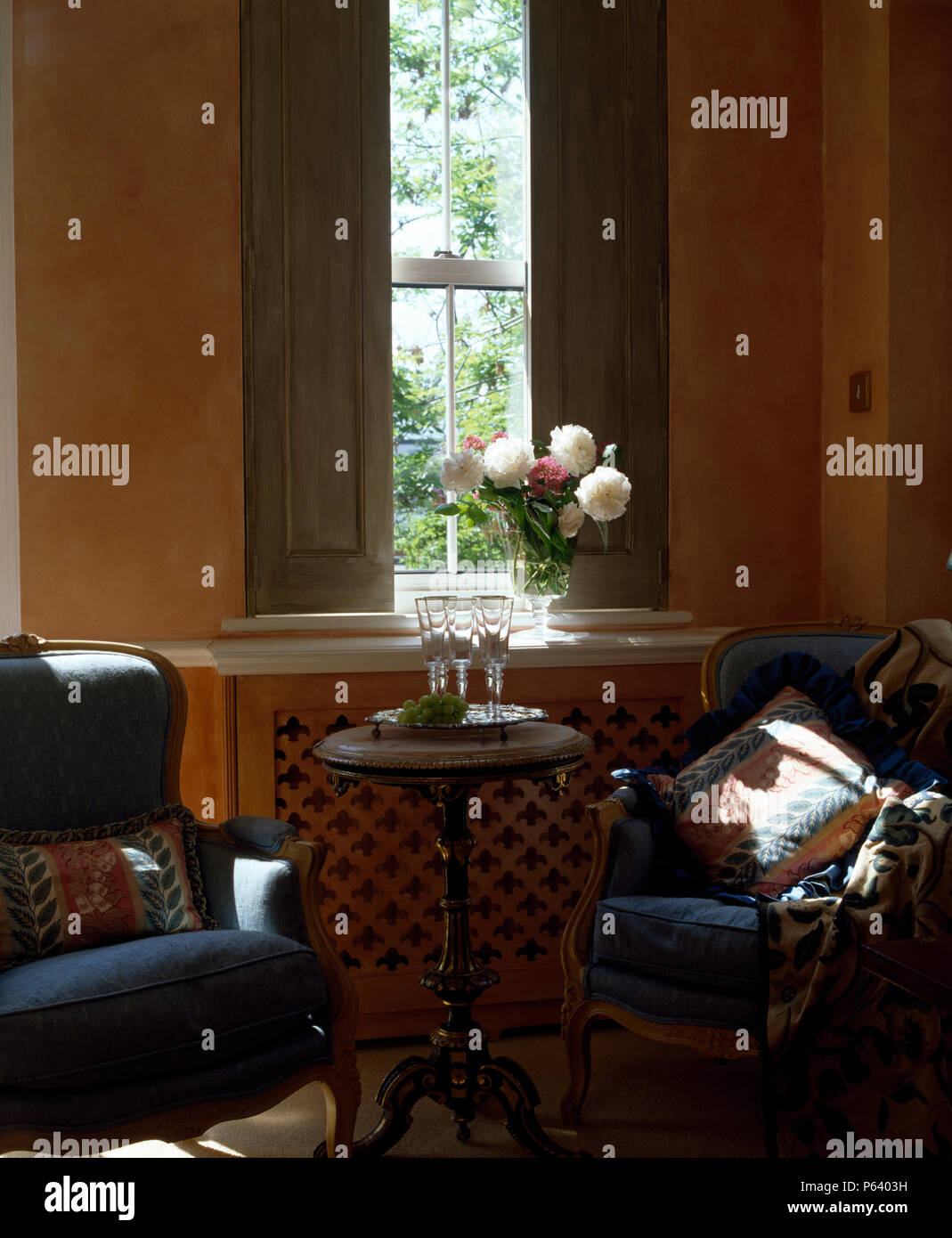 Des fauteuils bleus et petit table antique devant les fenêtres avec volets peints en vert Banque D'Images