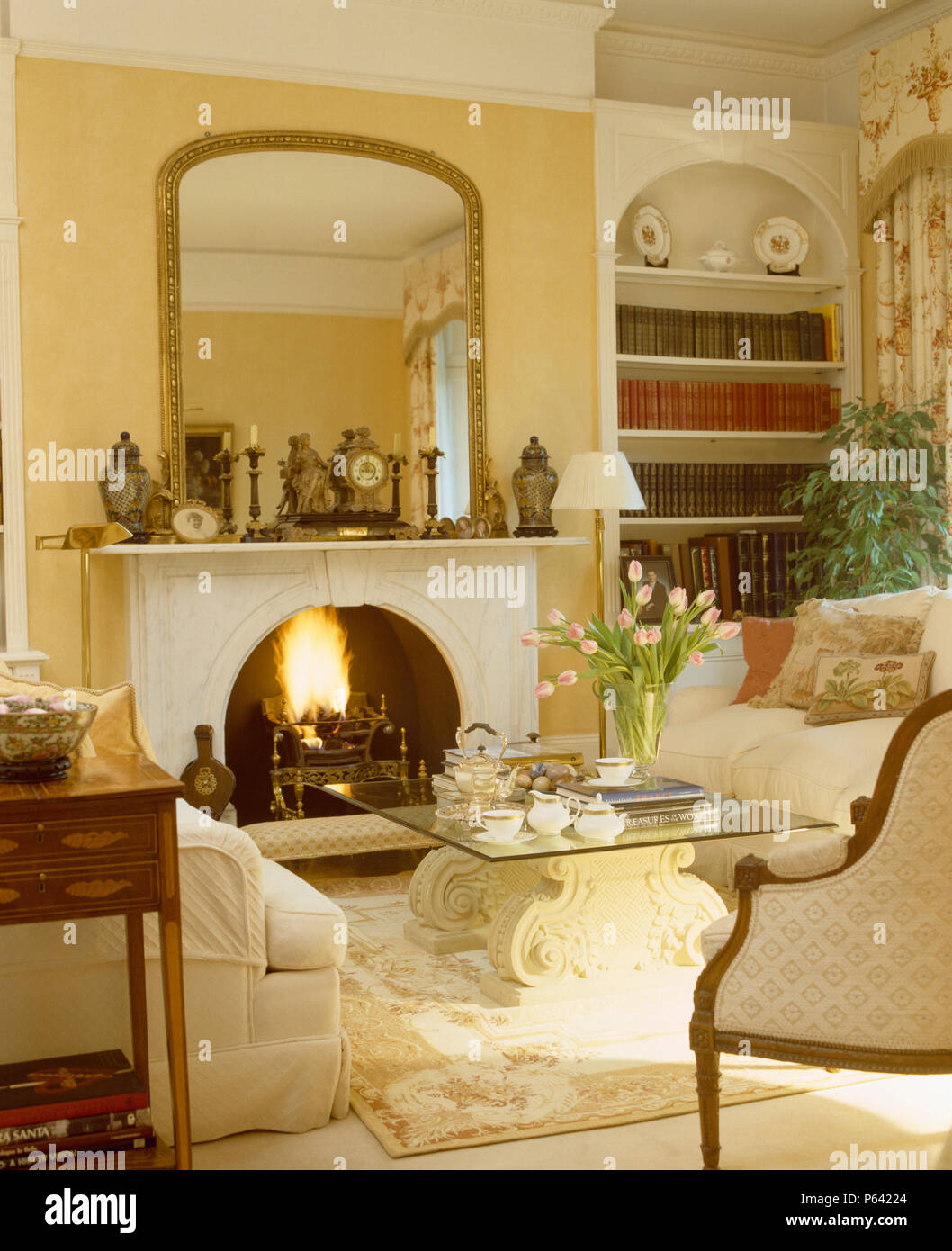 Grand miroir ancien doré au-dessus de cheminée en marbre avec feu allumé dans la salle de séjour avec le service à verre +table basse pierre Banque D'Images