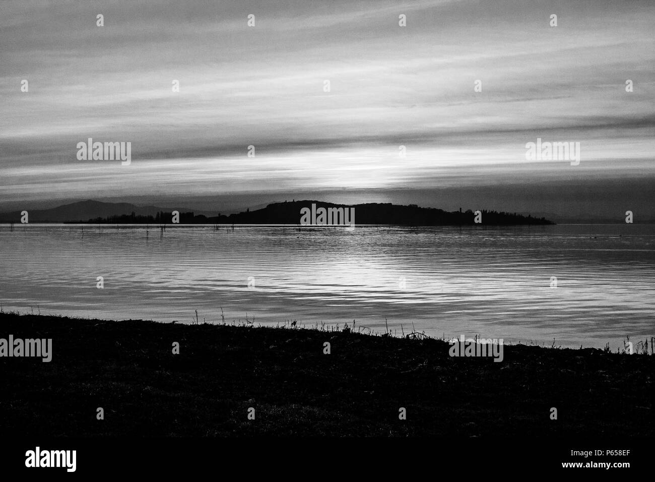 Une pousse d'un coucher de soleil sur un lac, avec de nombreuses lignes diagonales créées par les nuages et le littoral Banque D'Images