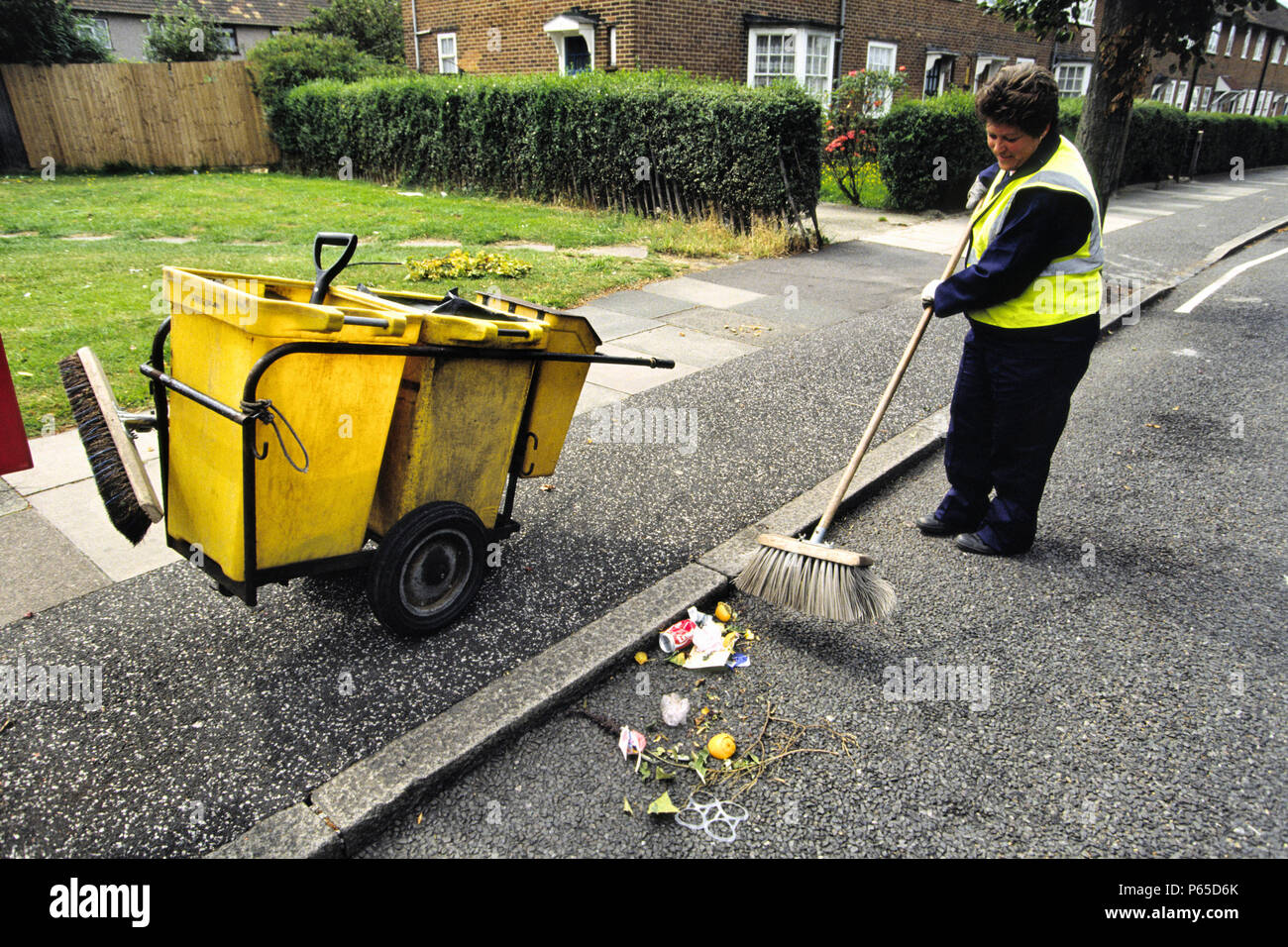 Une femme travaillant pour l'autorité locale (ou Conseil) utilise un balai pour balayer les ordures d'une rue résidentielle dans le London Borough of Greenwich, Royaume-Uni Banque D'Images