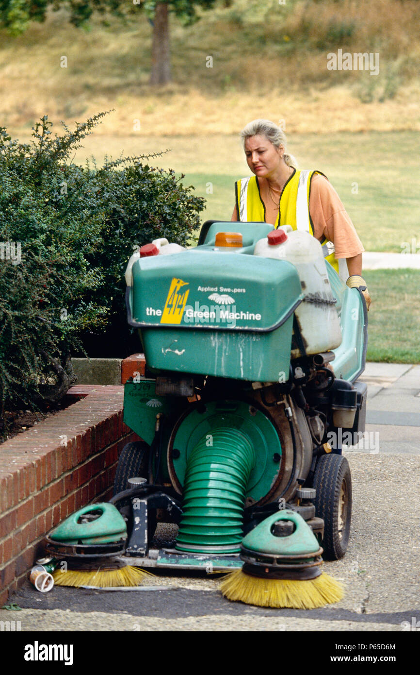 Une femme travaillant pour l'autorité locale (ou Conseil) utilise une machine verte pour balayer les ordures d'un quartier résidentiel de Greenwich, London, UK Banque D'Images