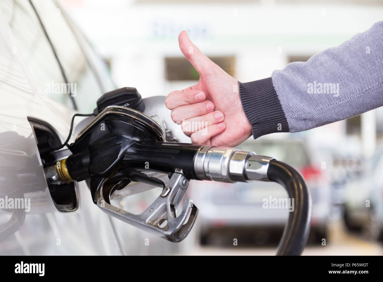 L'essence de l'essence ou pompée dans un véhicule à moteur voiture. Gros plan du mans hand showing thumb up geste, pomper l'essence dans la voiture à la station d'essence. Banque D'Images
