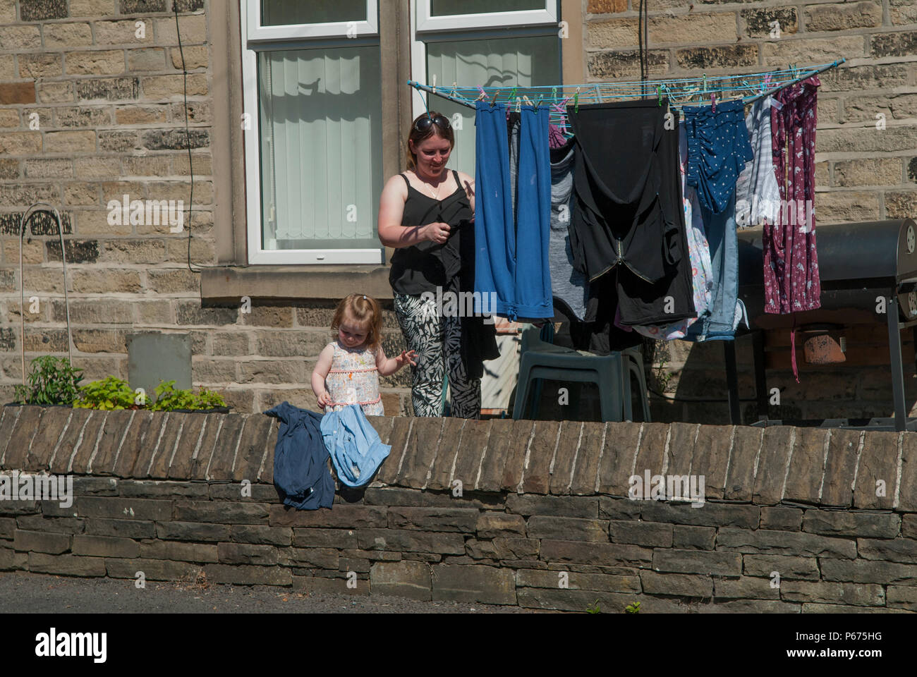 Enfant aidant sa mère avec la lessive de la famille accrochant des vêtements humides à sécher dans le jardin devant sur une corde à linge. nord de l'Angleterre années 2010 Royaume-Uni HOMER SYKES Banque D'Images