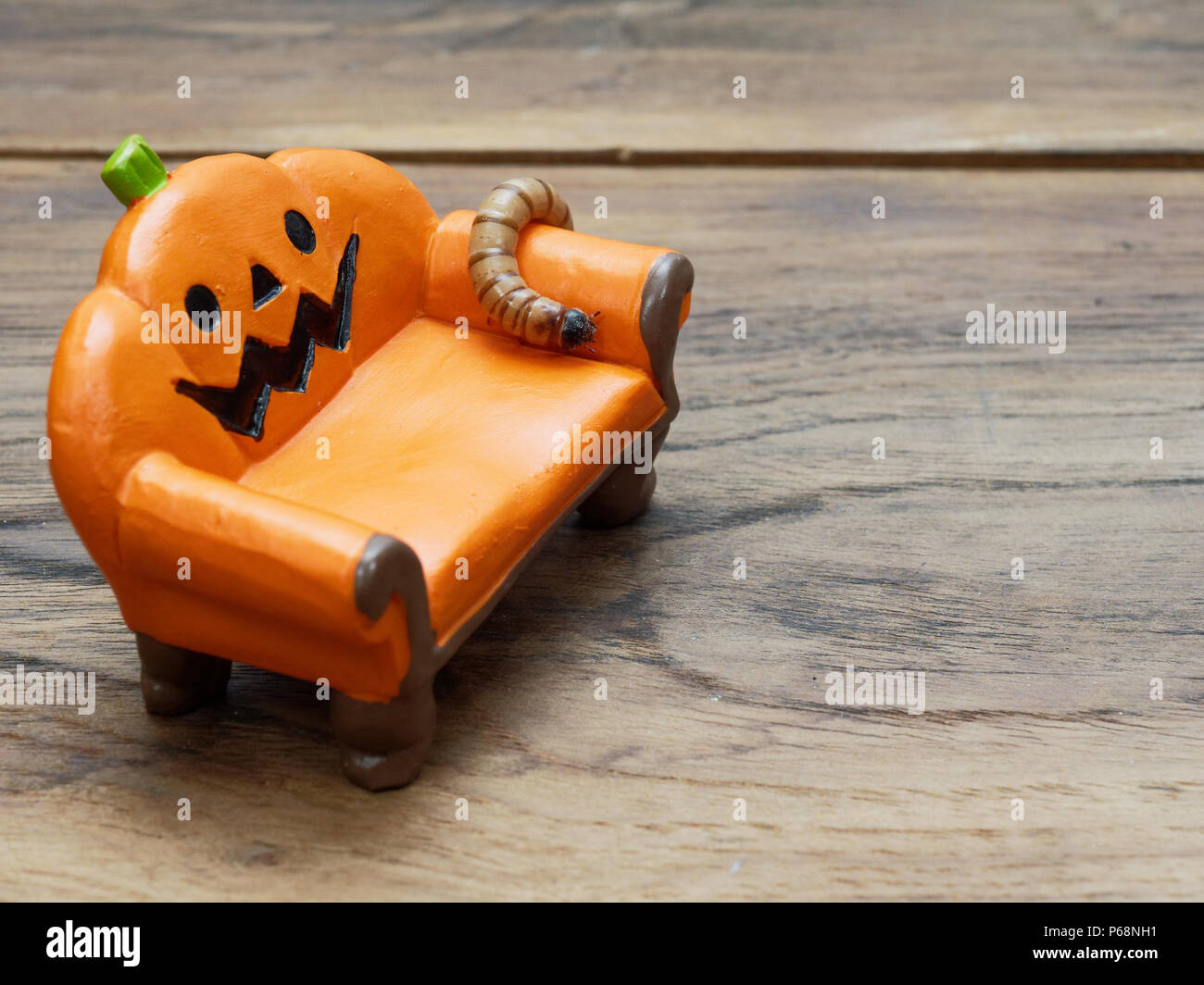 Super ou ver géant rampant sur l'orange citrouille céramique miniature canapé ou canapé sur la surface en bois foncé avec copie espace utilisé comme arrière-plan dans Halloween, ornement, célébration, et de la décoration Banque D'Images