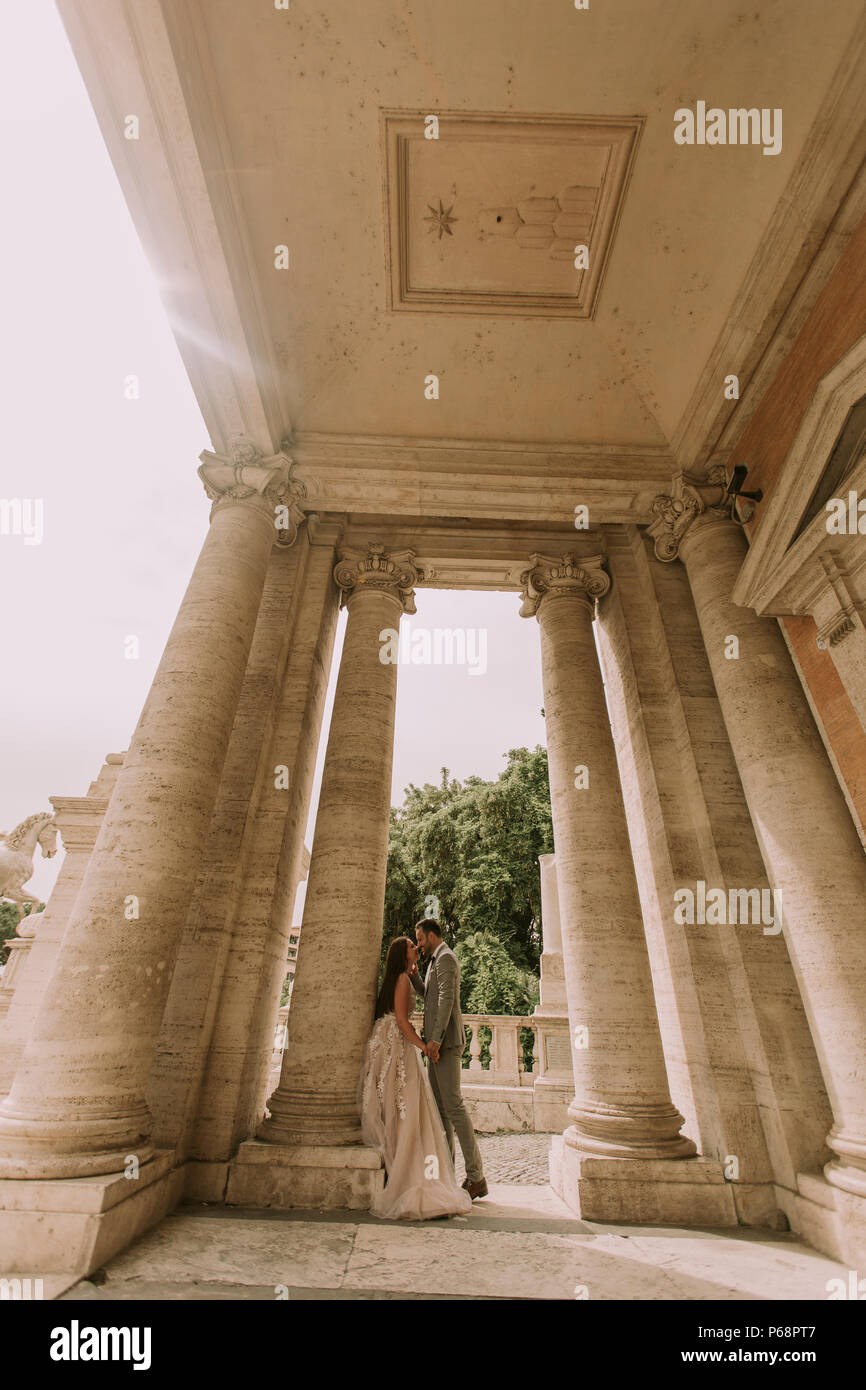 Young attractive couple nouvellement marié la marche et posant dans Rome avec belle architecture ancienne et sur l'arrière-plan le jour de leur mariage Banque D'Images