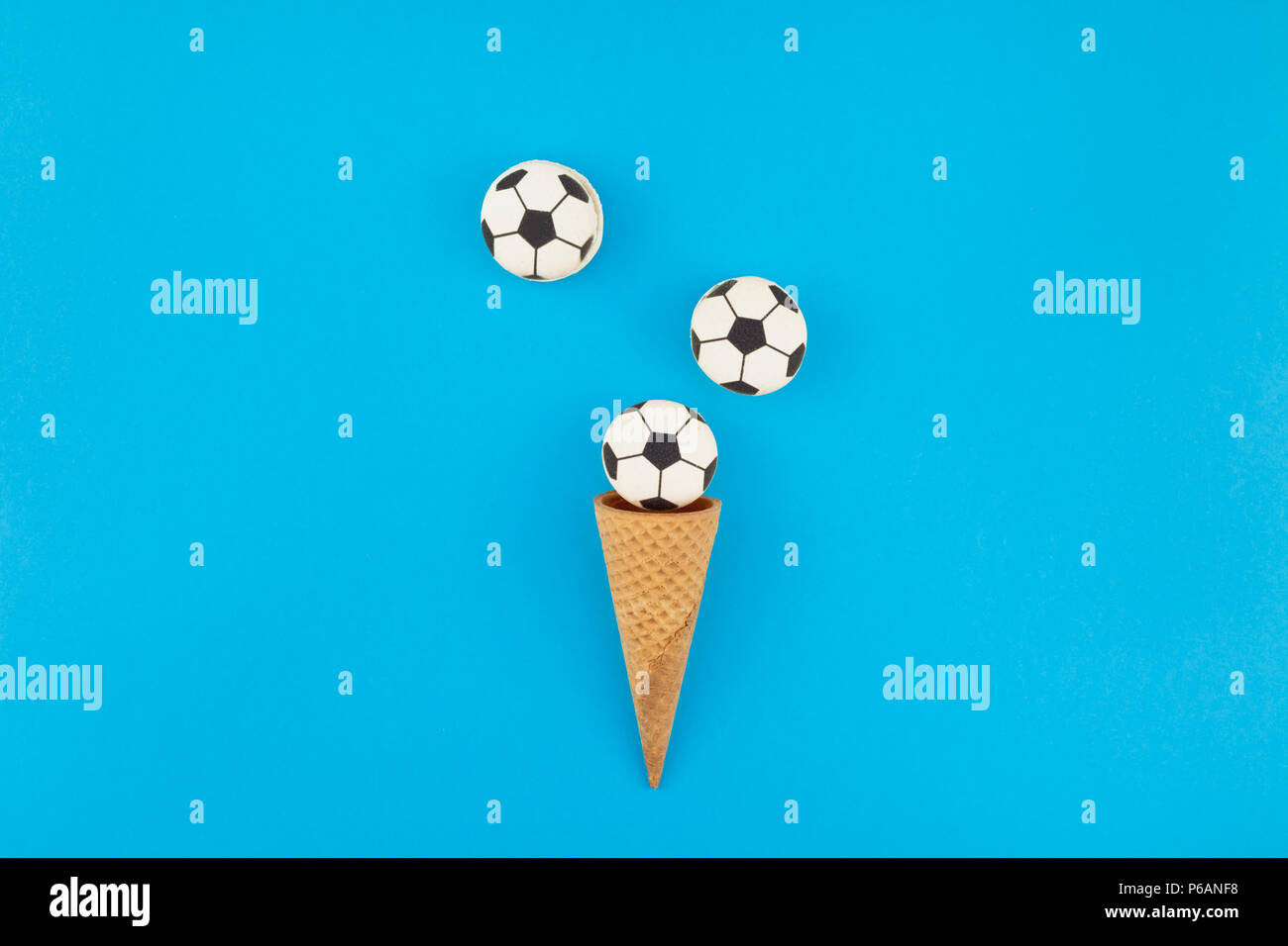 Télévision créative jeter Vue de dessus de la crème glacée cônes alvéolés avec des ballons de foot macarons sur fond bleu clair bold avec copie espace dans un style minimaliste, conce Banque D'Images