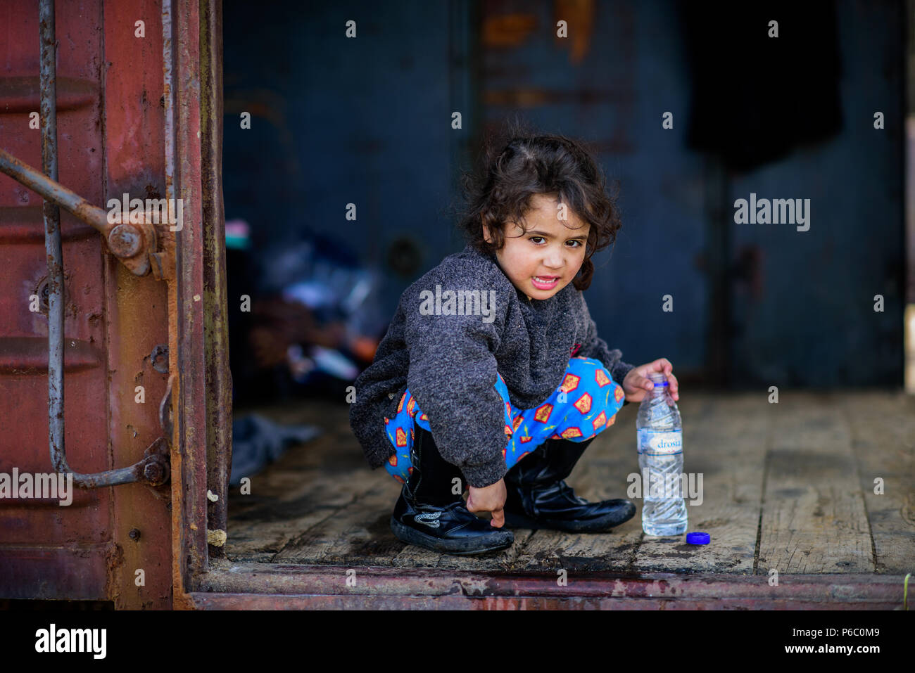 Petite fille joue avec une bouteille de l'eau dans l'ancien wagon de chemin de fer à la gare au camp de fortune de la frontière près de Greek-Macedonian e Banque D'Images