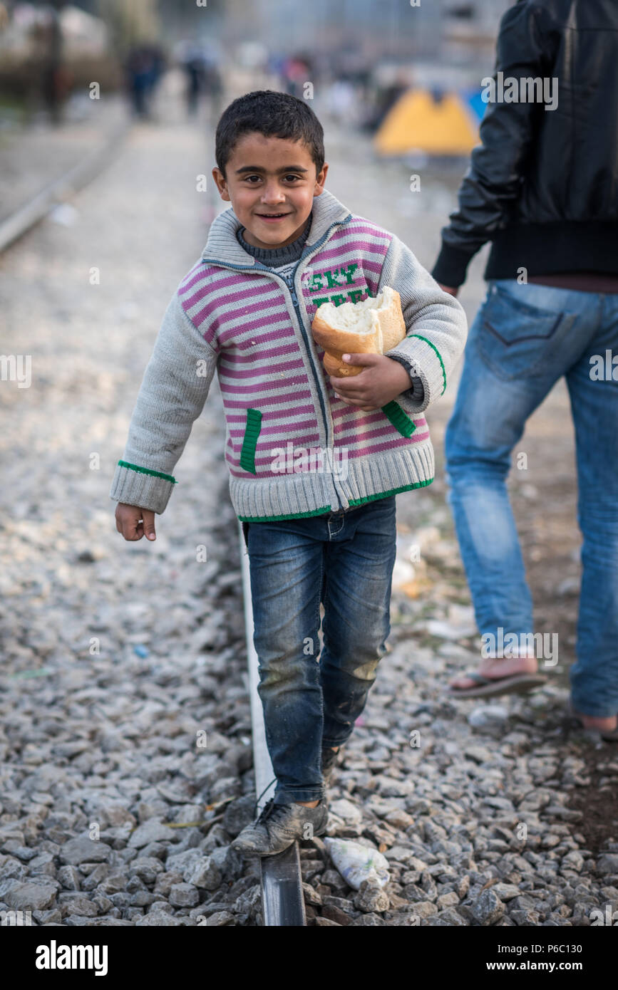 Jeune garçon réfugié promenades à travers la voie de chemin de fer avec un pain dans sa main à la gare de l'Greek-Macedonian frontière près du village grec de Id Banque D'Images