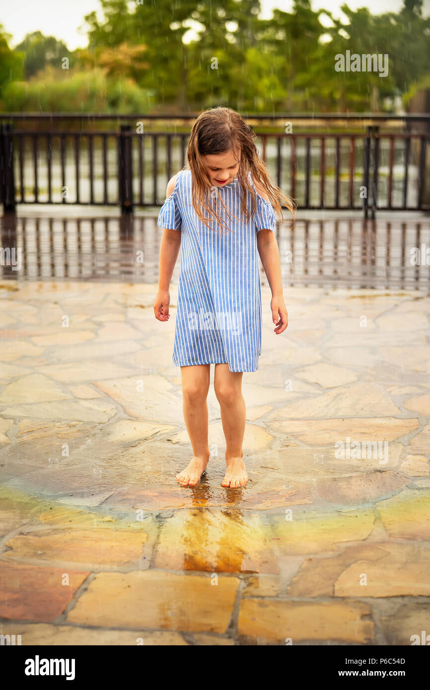 Petite fille jouant pieds nus à l'extérieur sous la pluie d'été Banque D'Images