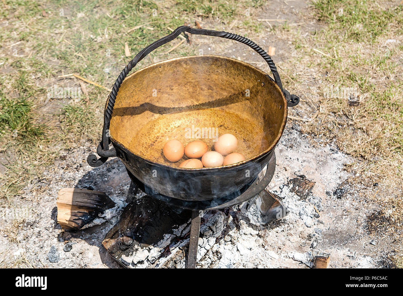 Oeufs dans le vieux chaudron métallique sur feu de camp Banque D'Images