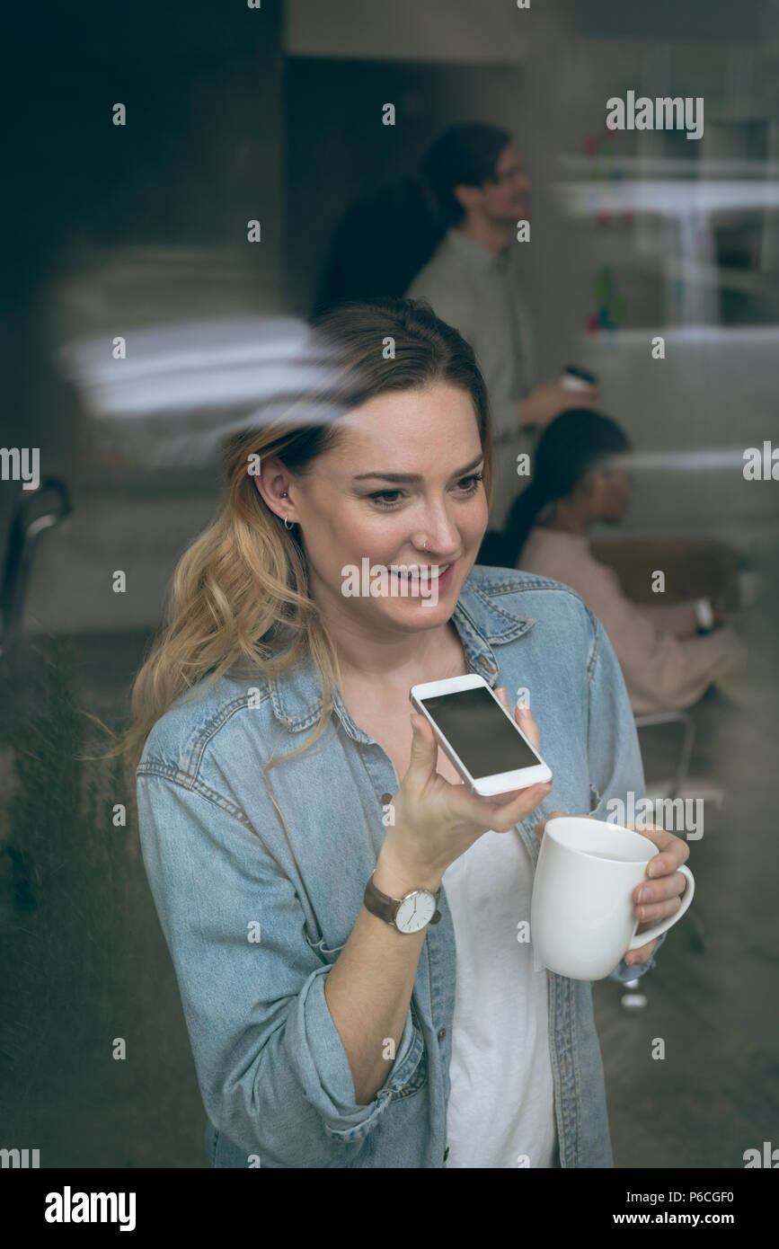 Female executive talking on mobile phone while having coffee Banque D'Images