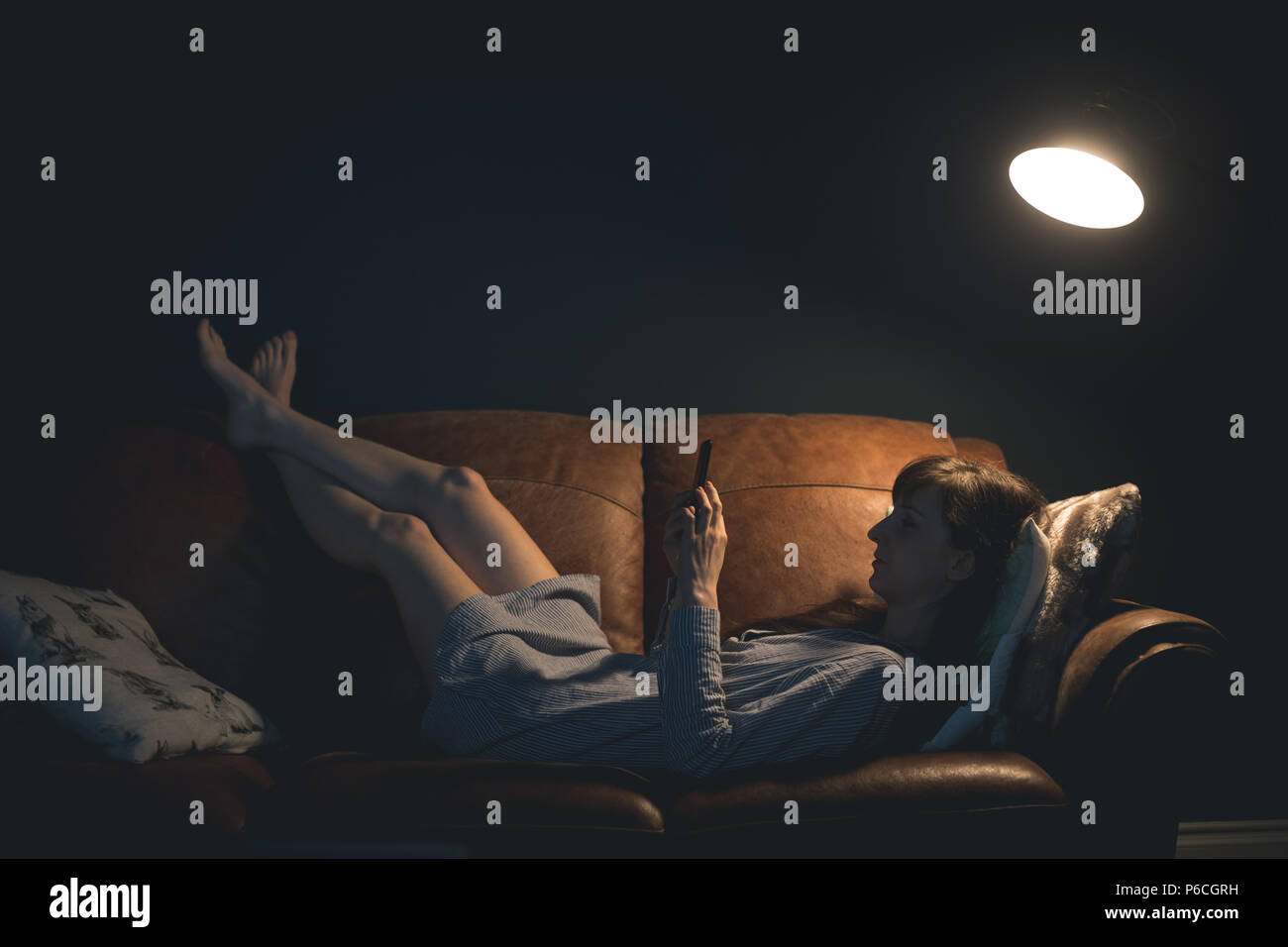 Woman using mobile phone while lying on sofa Banque D'Images