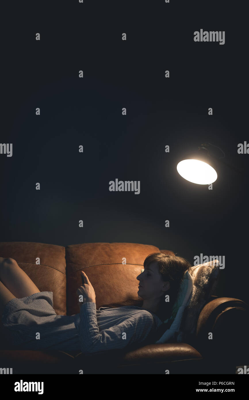 Woman using mobile phone while lying on sofa Banque D'Images
