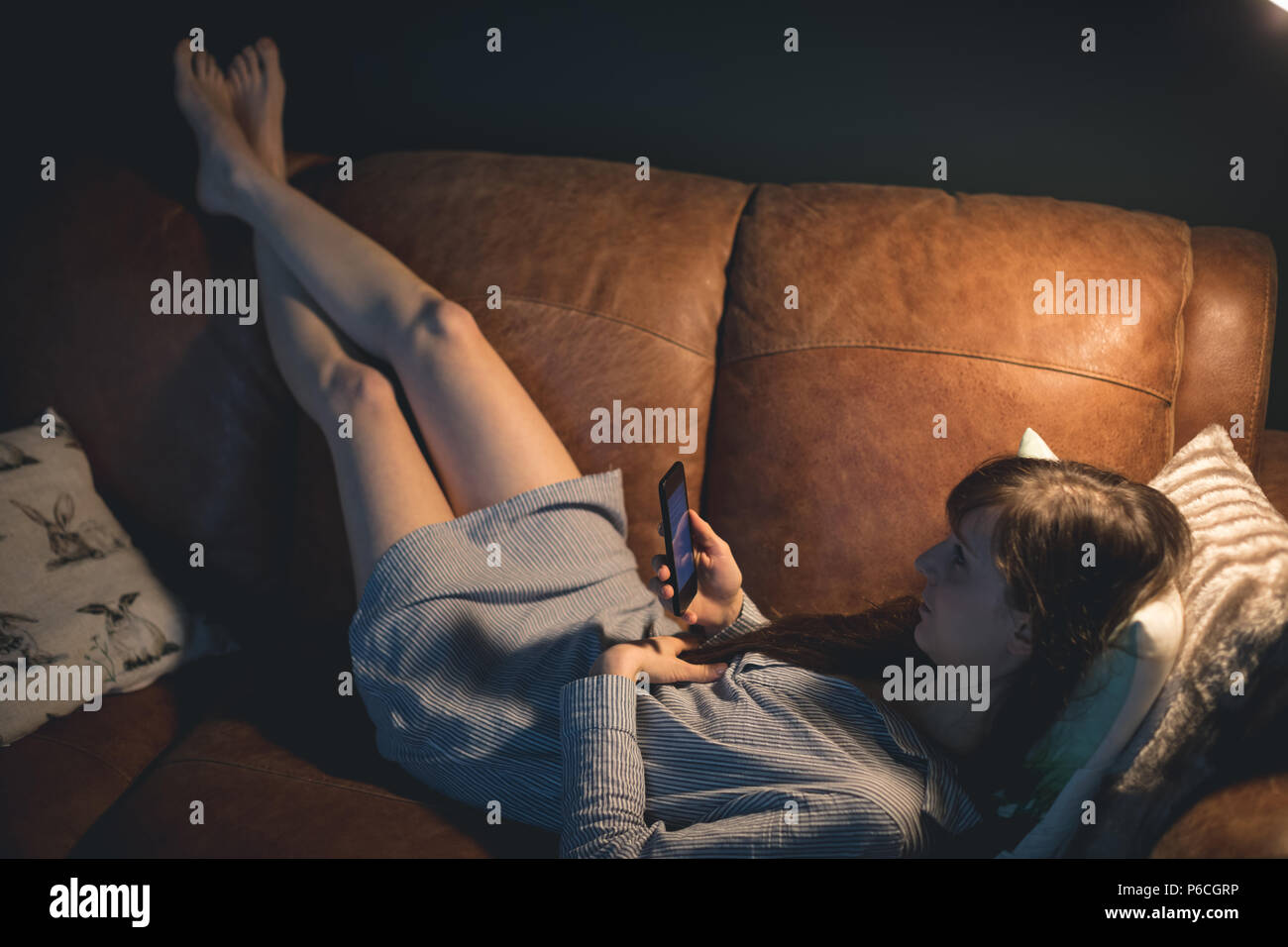 Woman using mobile phone while lying on sofa Banque D'Images