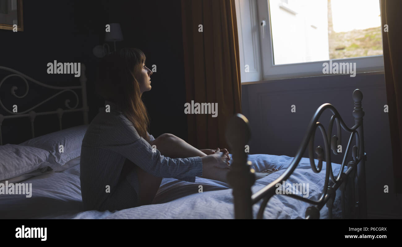 Femme regardant la fenêtre tandis qu'assis sur le lit Banque D'Images