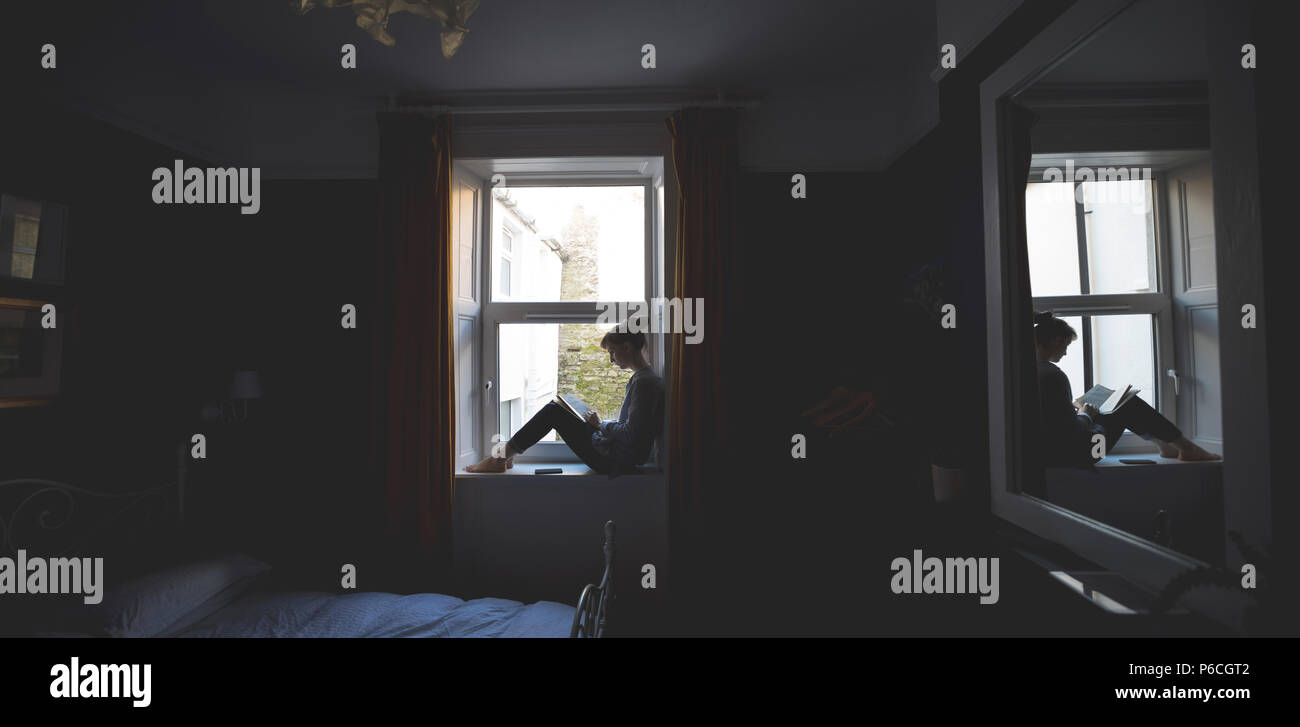 Woman Reading book on window sill Banque D'Images