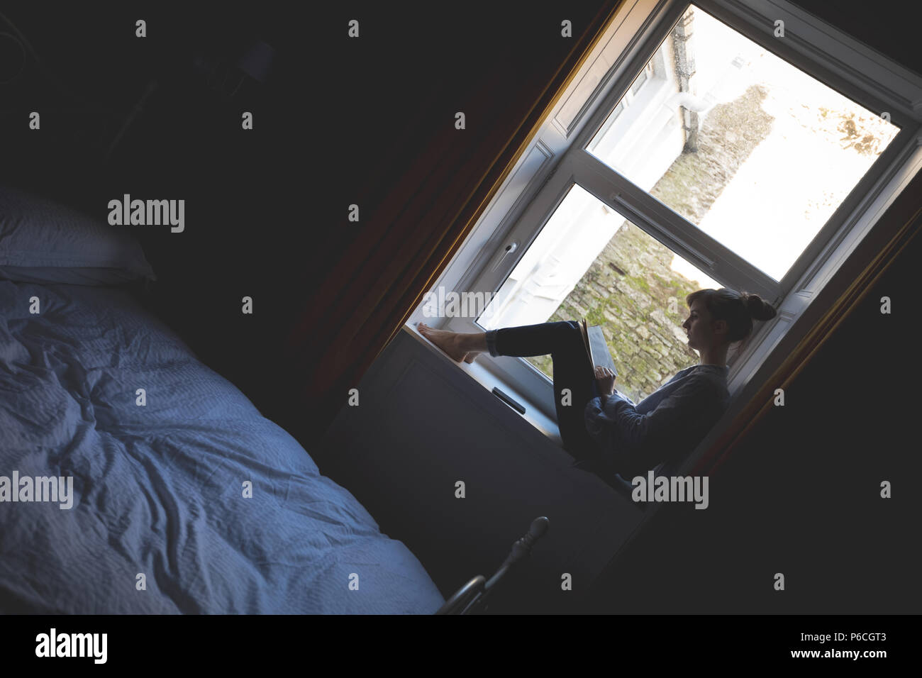 Woman Reading book on window sill Banque D'Images