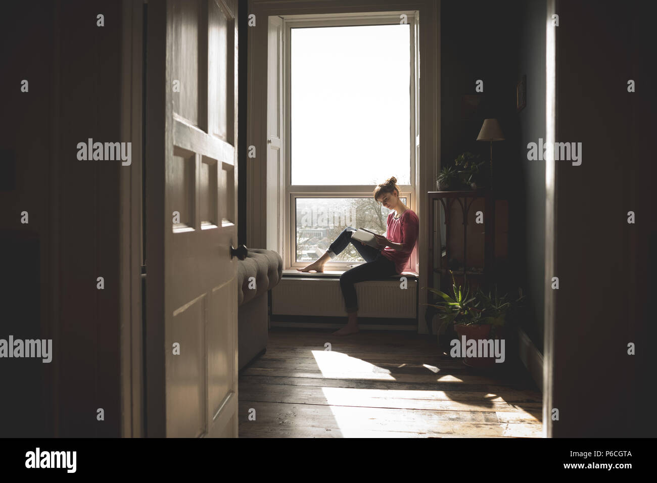 Woman Reading book on window sill Banque D'Images