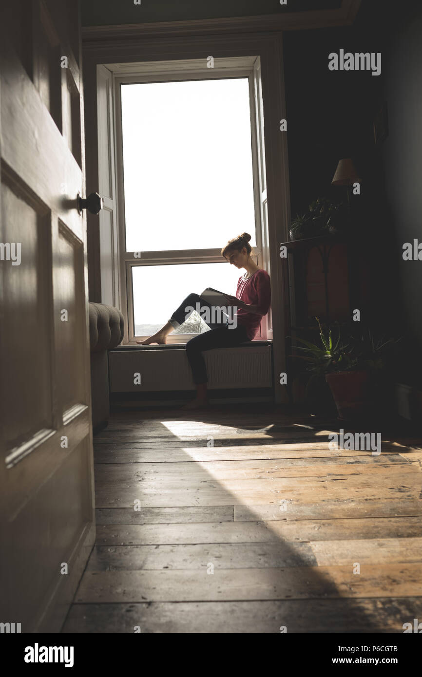 Woman Reading book on window sill Banque D'Images