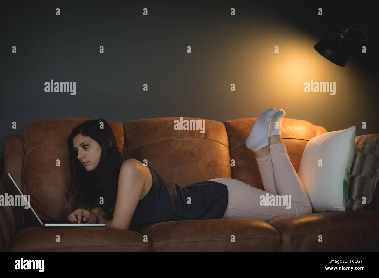 Woman using laptop while lying on sofa in living room Banque D'Images